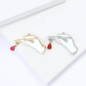 Detailed shot of creative alloy enamel hand holding scalpel brooch with red crystal drop.