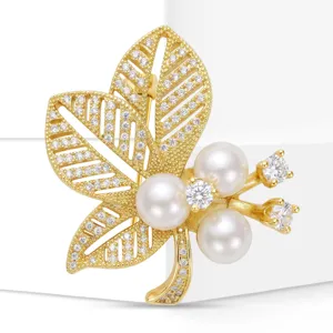 Primer plano detalle del elegante broche de hoja de perlas doradas con circonitas brillantes.