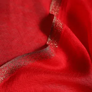 Red mulberry silk scarf detail close up, elegant gold woven border, traditional style.