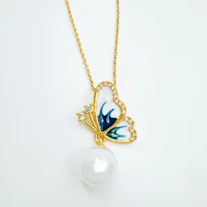 Detail view of gold plated butterfly pendant necklace with white enamel and dangling pearl.