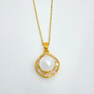 Close-up of gold-plated necklace pendant with central pearl and sparkling baguette stones.