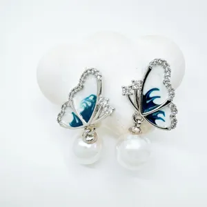 Elegant butterfly pearl earrings detail closeup, featuring sparkling cubic zirconia and blue oil drip.
