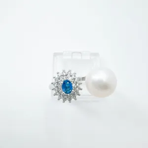 Elegante anillo abierto con racimo de circonitas azules y gran perla blanca en metal.