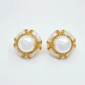 Detailed view of luxury pearl stud earrings with gold ornate metal frame and glitter design.