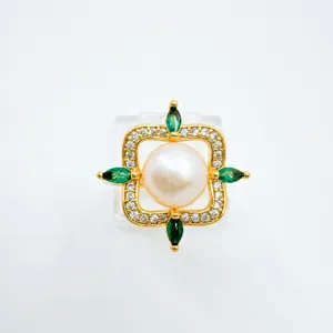 Nahaufnahme des Luxus-Perlenrings mit weißer Perle, goldenem Rahmen und grünen Schmucksteinen.