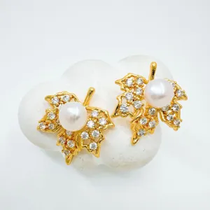Detailed shot of elegant gold plated maple leaf pearl stud earrings with sparkling zircons.