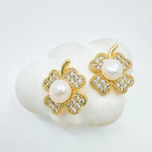 Close-up of elegant gold clover pearl earrings with sparkling zircon crystals on white display.