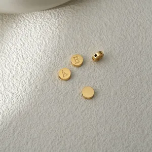 Perles disques lettres en acier inoxydable doré vue de détail, bijoux minimalistes.