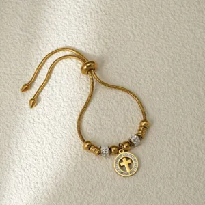 Detalle de pulsera de acero inoxidable dorada ajustable con colgante de cruz de diamantes y cuentas.