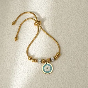 Detalle de pulsera de acero inoxidable dorado con abalorio de mal de ojo y cuentas brillantes.