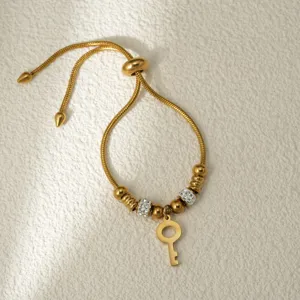 Elegante pulsera ajustable de acero dorado con abalorios de cristal y colgante de llave.