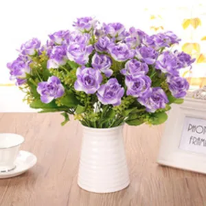 Vista dettagliata di un mazzo di rose viola artificiali in un vaso di ceramica bianca sul tavolo.