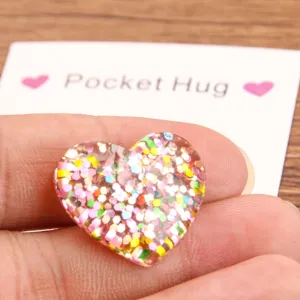 Detailed close-up view of a colorful glitter resin heart pocket hug token with card.