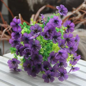 Close-up detail shot of purple artificial flower bouquet with green leaves for home decor setup.