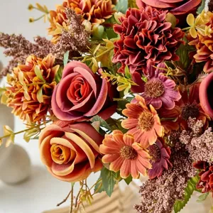 Nahaufnahme eines herbstlichen Kunstblumenstraußes mit Rosen und bunten Gänseblümchen.