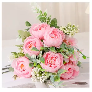 Close-up detail shot of pink artificial peony bouquet with green leaves and white berries decor.