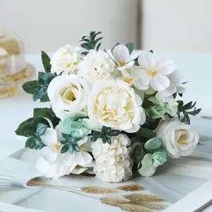 Close-up detail of elegant white artificial flower bouquet with roses and green leaves.