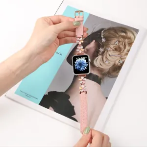 Dettaglio in primo piano del cinturino Apple Watch in pelle rosa con ciondoli di fiori.
