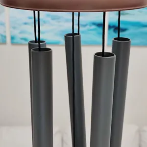 Close-up detail of metal wind chime tubes with hanging cords and top disc, patio decor.