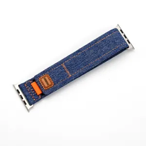 Gros plan sur le bracelet de montre connectée en denim bleu avec coutures orange et métaux.