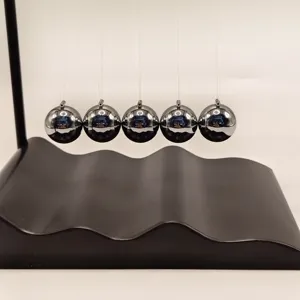 Close-up detail of Newton's cradle science toy with black metal balls and wave base.