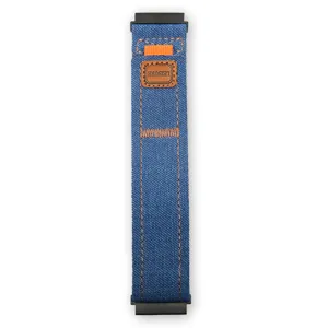 Dettaglio cinturino per orologio in tela jeans blu con cuciture arancioni e etichetta.