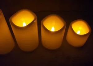 Detailansicht zylindrischer LED Kunststoff Kerzen mit warmem gelben Licht im dunklen Raum.