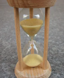 Wooden sand glass timer detail shot showing natural wood texture and yellow fine sand inside.
