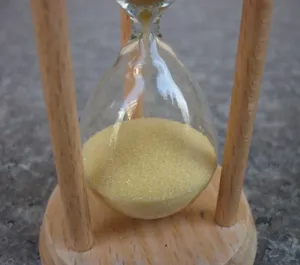 Close-up detail of the wooden frame and clear glass hourglass with yellow sand inside.