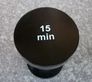 Nahaufnahme Detailansicht der schwarzen runden Holz 15 Minuten Sanduhr Oberflaeche mit Text