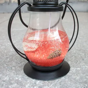 Close-up detail of creative red gel wax candle holder with decorative seashells and sand inside.