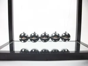 Close-up of Newton's cradle with chrome spheres and mirrored base for office decor.