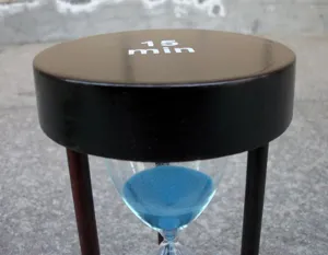 Detailaufnahme einer hölzernen 15-Minuten-Sanduhr mit blauem Sand als Tischdekoration.
