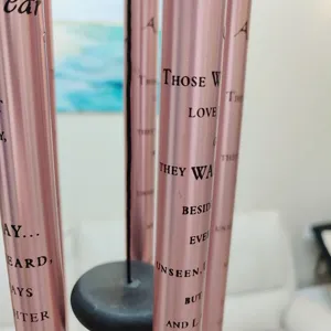 Close-up detail view of pink metal wind chime tubes featuring engraved memorial English text.