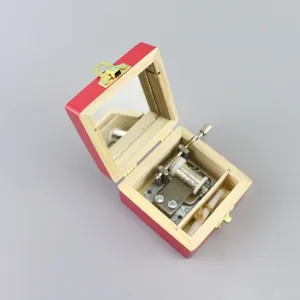 Hand crank wooden music box with red exterior finish and interior mirror for holiday gifts.