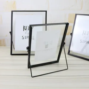 Close up of double-sided rotating glass photo frame with black metal border for desktop decor.
