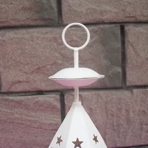 Close-up detail of white metal candle holder with star cutouts and ring hook top design.