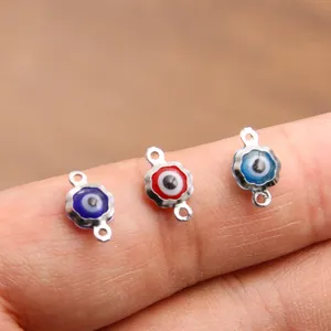 Détail de connecteur pendentif fleur œil turc en acier, vue macro sur le doigt.