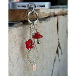 Detailed shot of cute red mushroom and flower metal phone charm pendant with snake chain aesthetic.