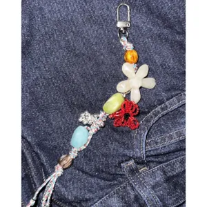 Beaded phone charm detail shot, colorful floral elements, handmade aesthetic strap for bags.