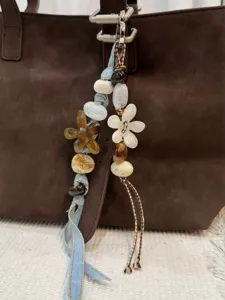 Close-up detail shot of a beaded bag charm with denim fabric, resin flowers, and braided cord.