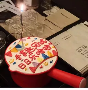 Gedetailleerd overzicht van een creatieve rode lepelvormige verjaardagstaart met brandende kaars.