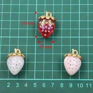 Primer plano detalle del colgante de fresa 3D con estrás, borde de metal dorado, fino diseño.