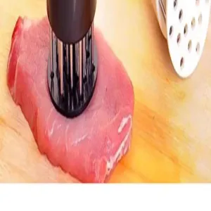 Dettaglio ravvicinato di batticarne in acciaio inox che fora la carne cruda sul tagliere.