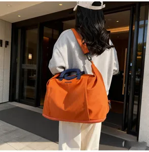 Vue détaillée du grand sac de voyage orange, doté de poignées solides et d'une bandoulière.
