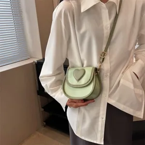 Nahaufnahme einer hellgrünen Ledertasche im Sattel-Design mit süßem Herzdetail.