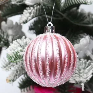 Pallina di Natale rosa costmata con dettagli di glitter argentati appesa su albero innevato