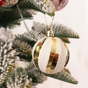 Vista detallada de bola de Navidad a rayas blancas y doradas colgada en una rama.