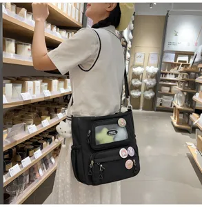 Schwarze Schultertasche aus Canvas mit Sichtfenster und Pins, ideal für den Alltag im Streetstyle.