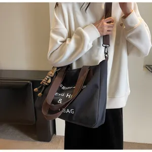 Lässige schwarze Canvas-Tasche für Damen, große Umhängetasche mit Buchstaben und Anhänger.
